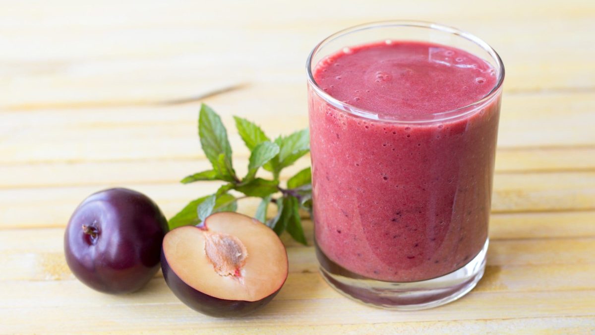 Pflaumen-Smoothie mit Heidelbeere, Minze und Basilikum in einem Glas auf Holztisch. Im Bild frische Minze und Pflaumen. Draufsicht.