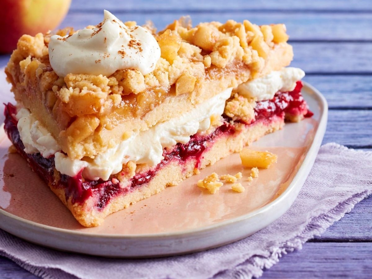 Ein Stück Prasselkuchen mit Vanille-Mascarpone-Creme auf einem Teller, darunter ein Tuch, blauer Holzuntergrund.