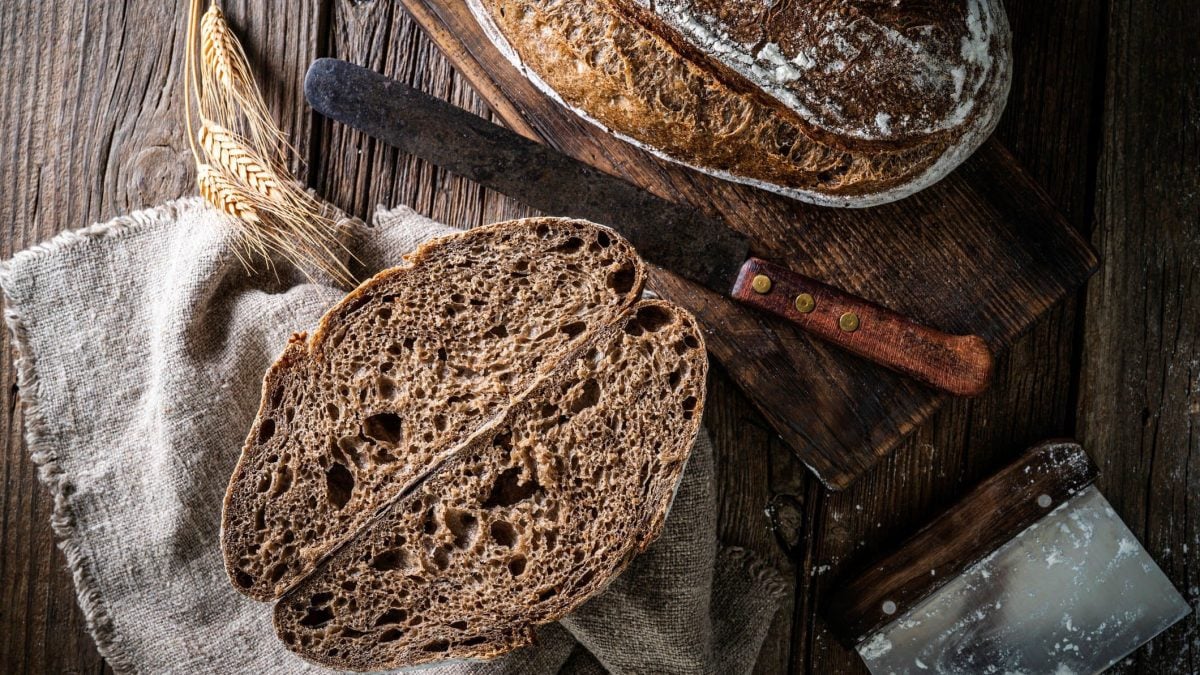 Sauerteigbrot Rezept zum Nachbacken aufgeschnittenes Sauerteigbrot auf Holztisch. Im Bild Stofftuch und ein Messer mit Holzgriff.