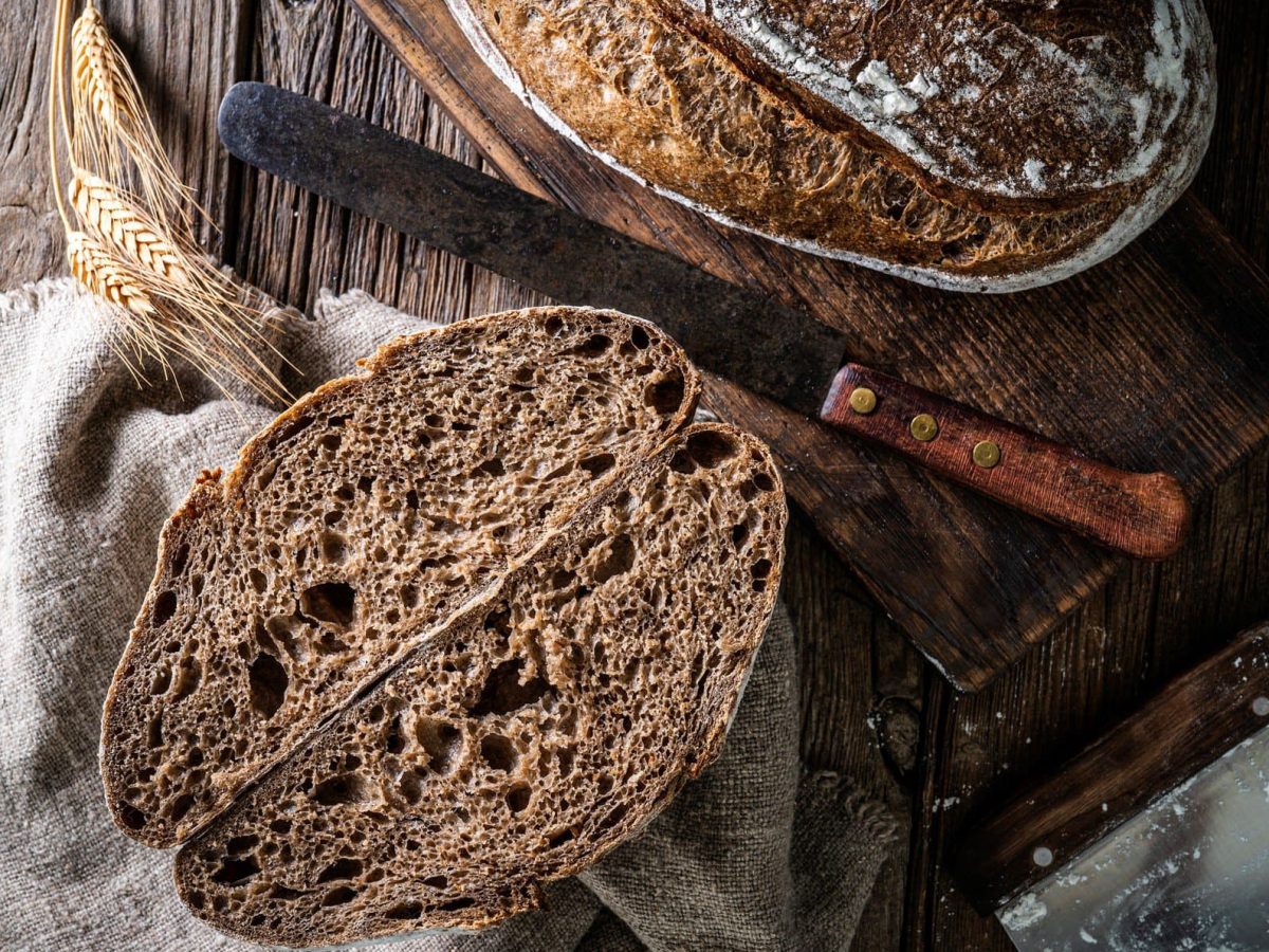 Sauerteigbrot Rezept zum Nachbacken aufgeschnittenes Sauerteigbrot auf Holztisch. Im Bild Stofftuch und ein Messer mit Holzgriff.