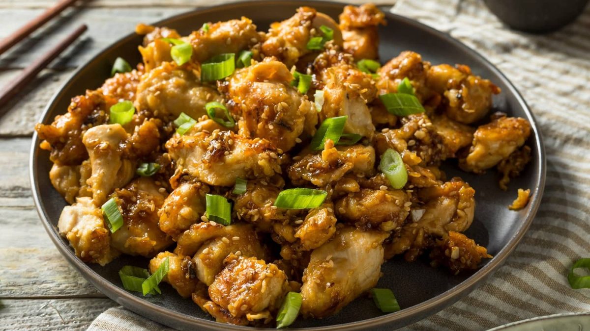 Ein Teller mit Sesame Chicken auf einem hellen Holztisch.