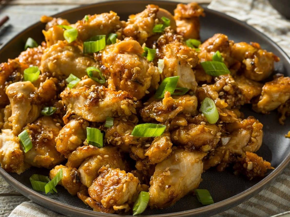 Ein Teller mit Sesame Chicken auf einem hellen Holztisch.