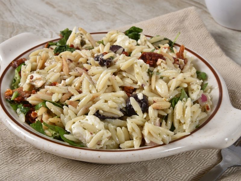 Ein tiefer Teller mit Orzo-Pasta mit getrockneten Tomaten und Mozzarella.