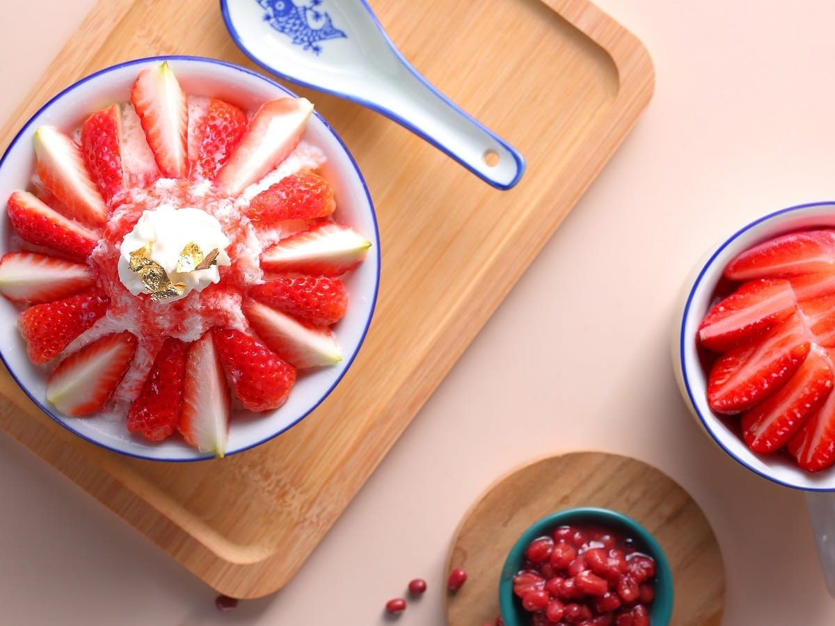 Ein Holztablett mit Strawberry Bingsu auf einem rosafarbenen Untergrund.