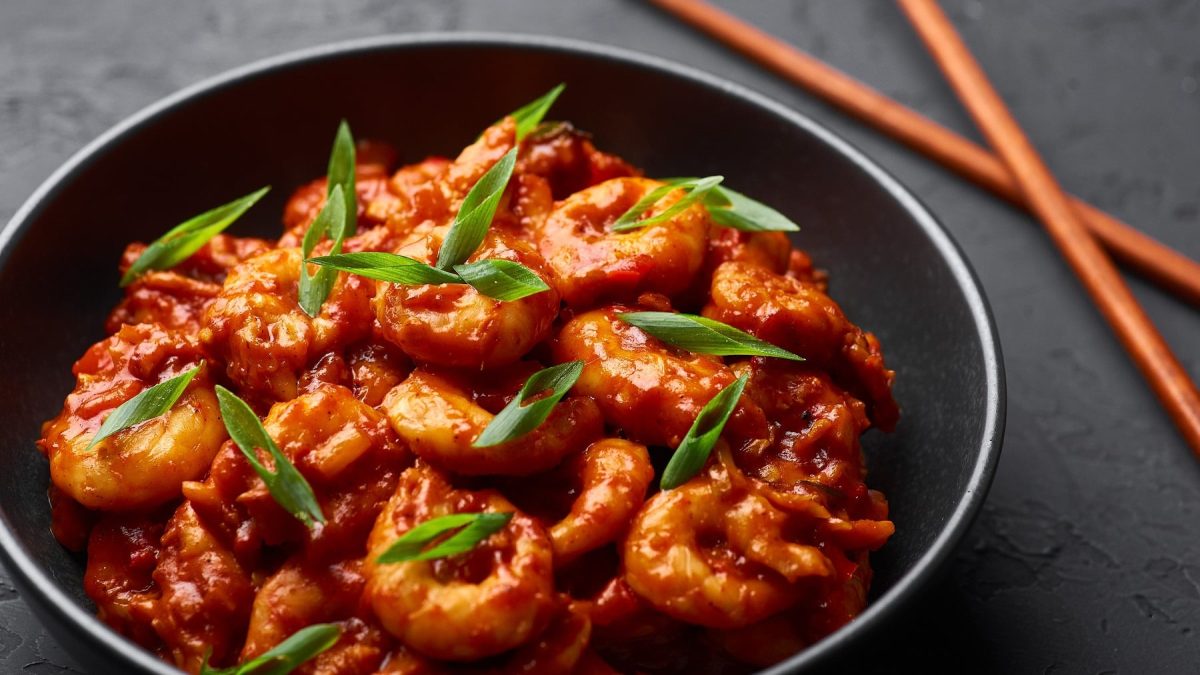 Ein schwarzer Teller mit den Sichuan-Garnelen auf dunklem Untergrund mit braunen Essstäbchen.