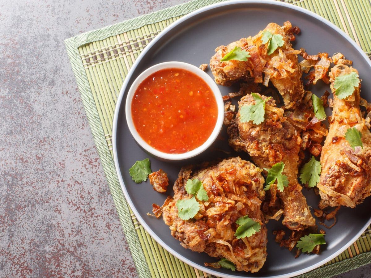 Thai Thai Fried Chicken Hat Yai Style mit Röstzwiebeln und Sauce auf grauem Teller, Matte und grauem Tisch. Draufsicht.