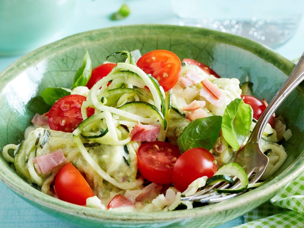 In einer Schüssel ist eine Portion Zucchini-Spaghetti angerichtet. Sie ist mit Tomaten und Basilikum verfeinert.