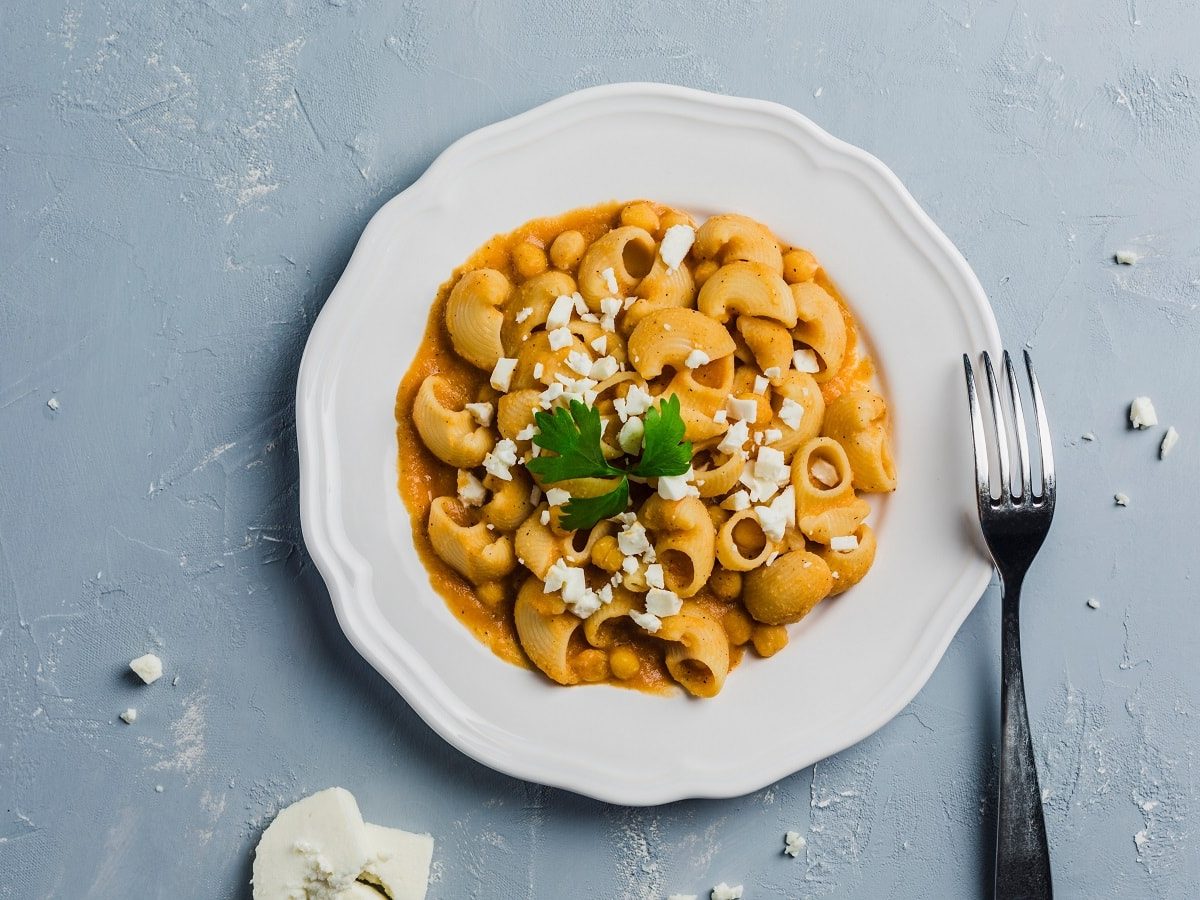 Ein weißer Teller mit Pasta mit Kichererbsensauce auf einem grauen Tisch.