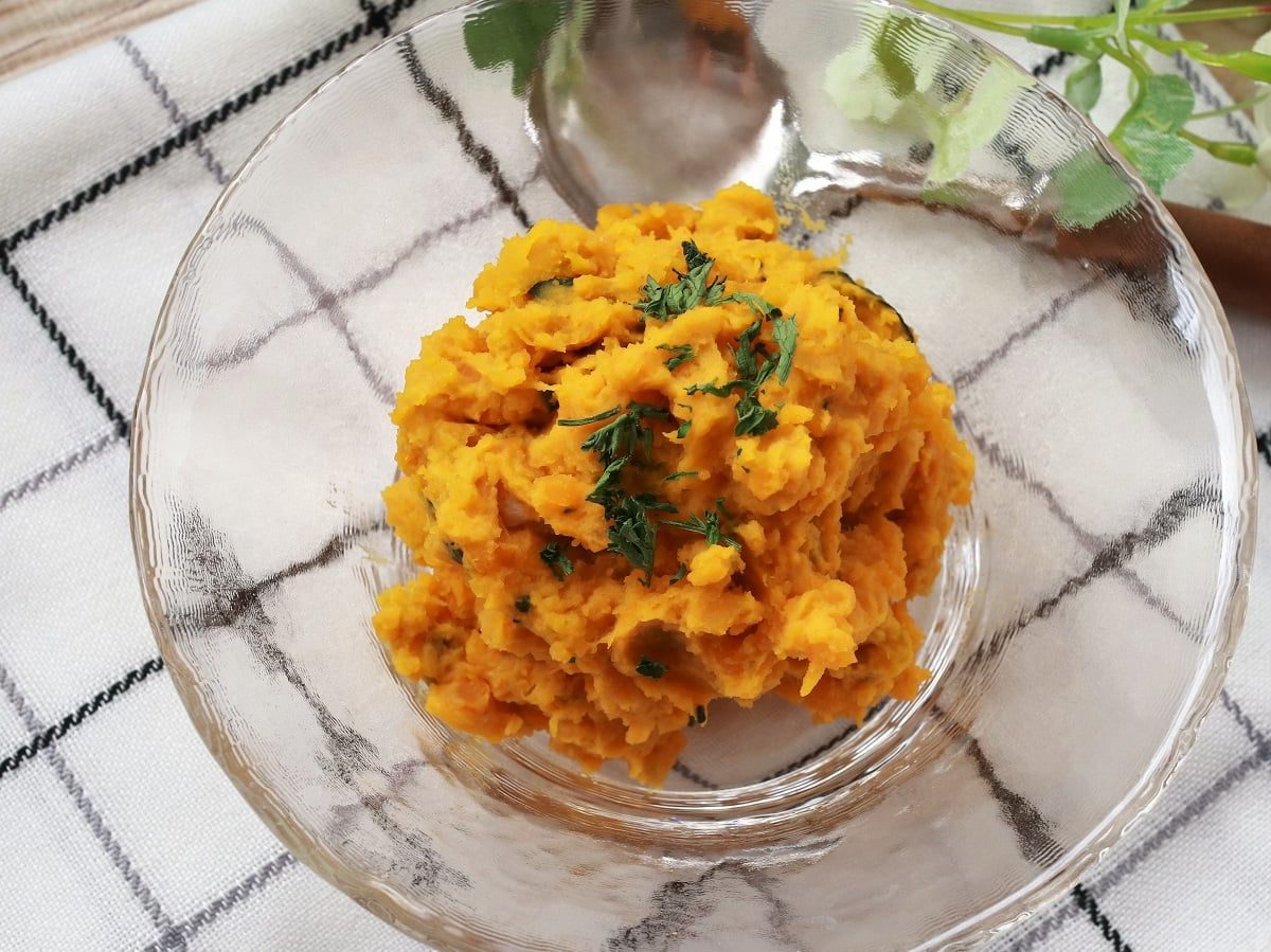 Eine Glasschüssel mit Kabocha-Salat auf einem karierten Geschirrtuch.