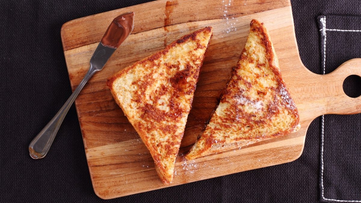 Ein French Toast mit Schokolade und Banane auf einem Holzbrett.