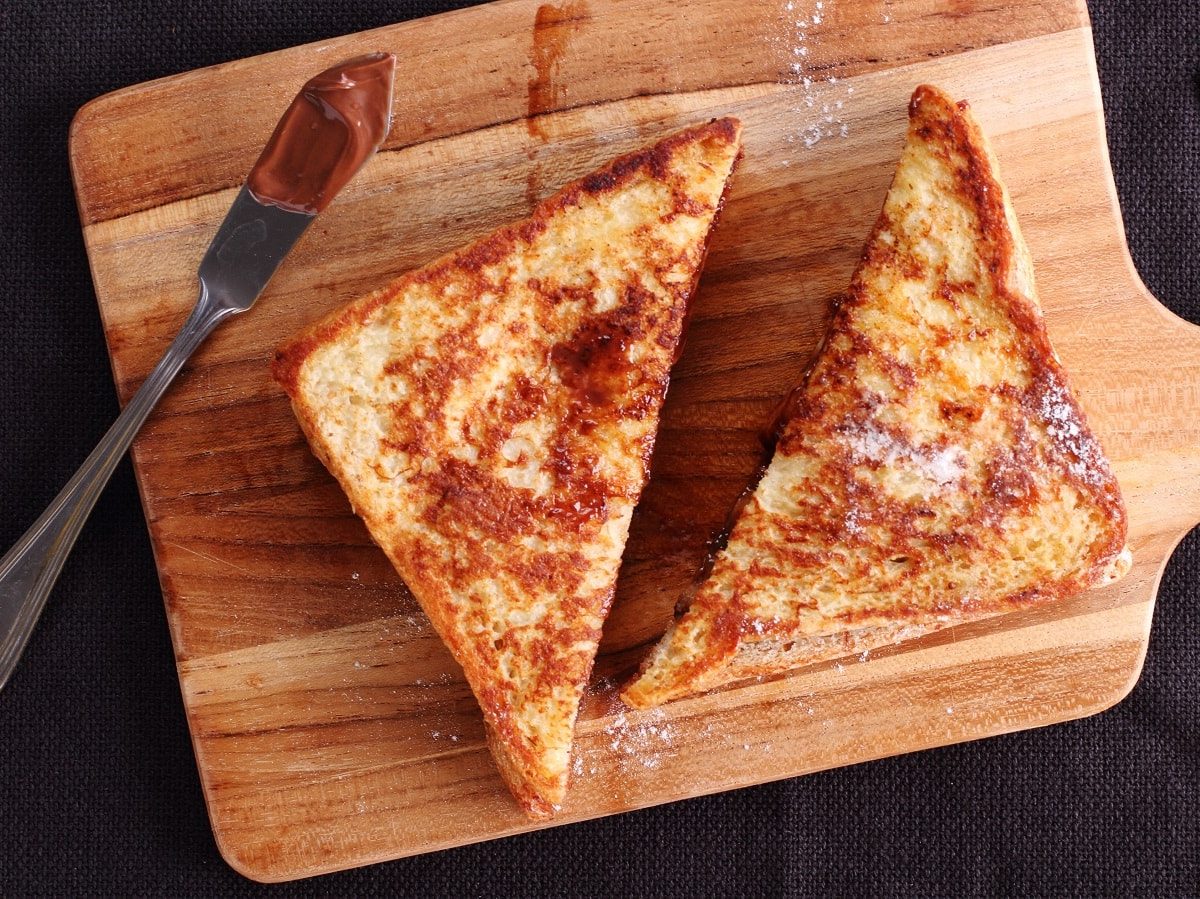 Ein French Toast mit Schokolade und Banane auf einem Holzbrett.