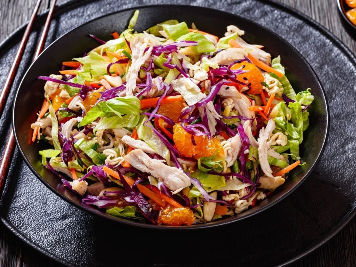 Der asiatische Kohlsalat auf einem schwarzen Teller und schwarzem Tisch von schräg oben fotografiert.