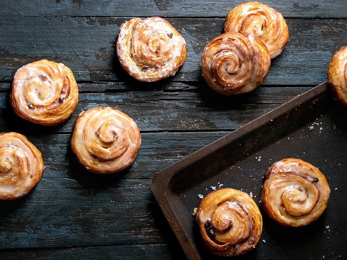 Blätterteig-Schnecken mit Erdnussmus und Marmelade auf einem hölzernen, dunklen Hintergrund. Rechts ein schwarzes Backblech.