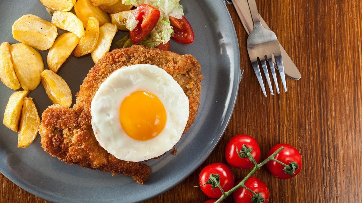 Ein blauer flacher Teller mit einem Hamburger Schnitzel darauf.