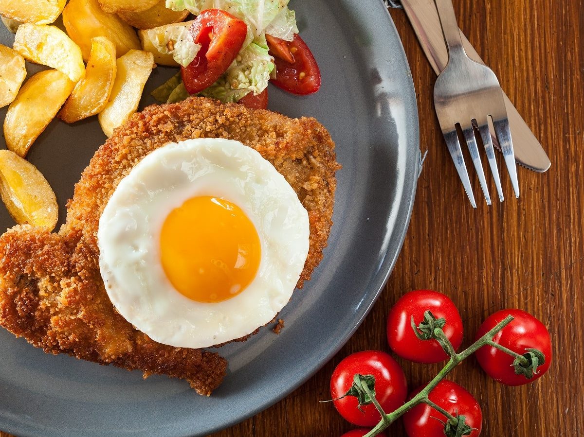 Ein blauer flacher Teller mit einem Hamburger Schnitzel darauf.