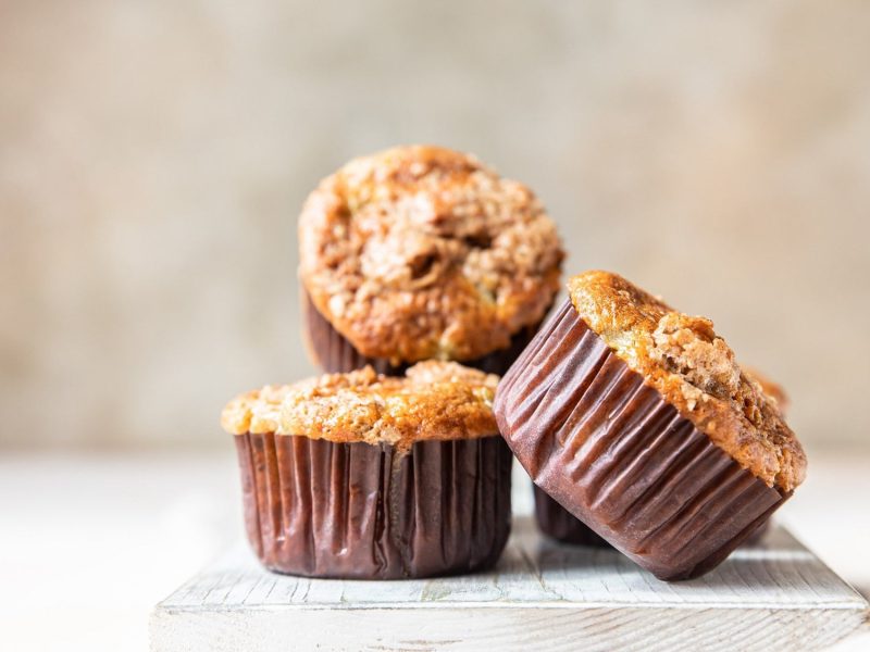 3 Kürbismuffins mit Streuseln auf einem weoßen Brett vor hellem Hintergrund.