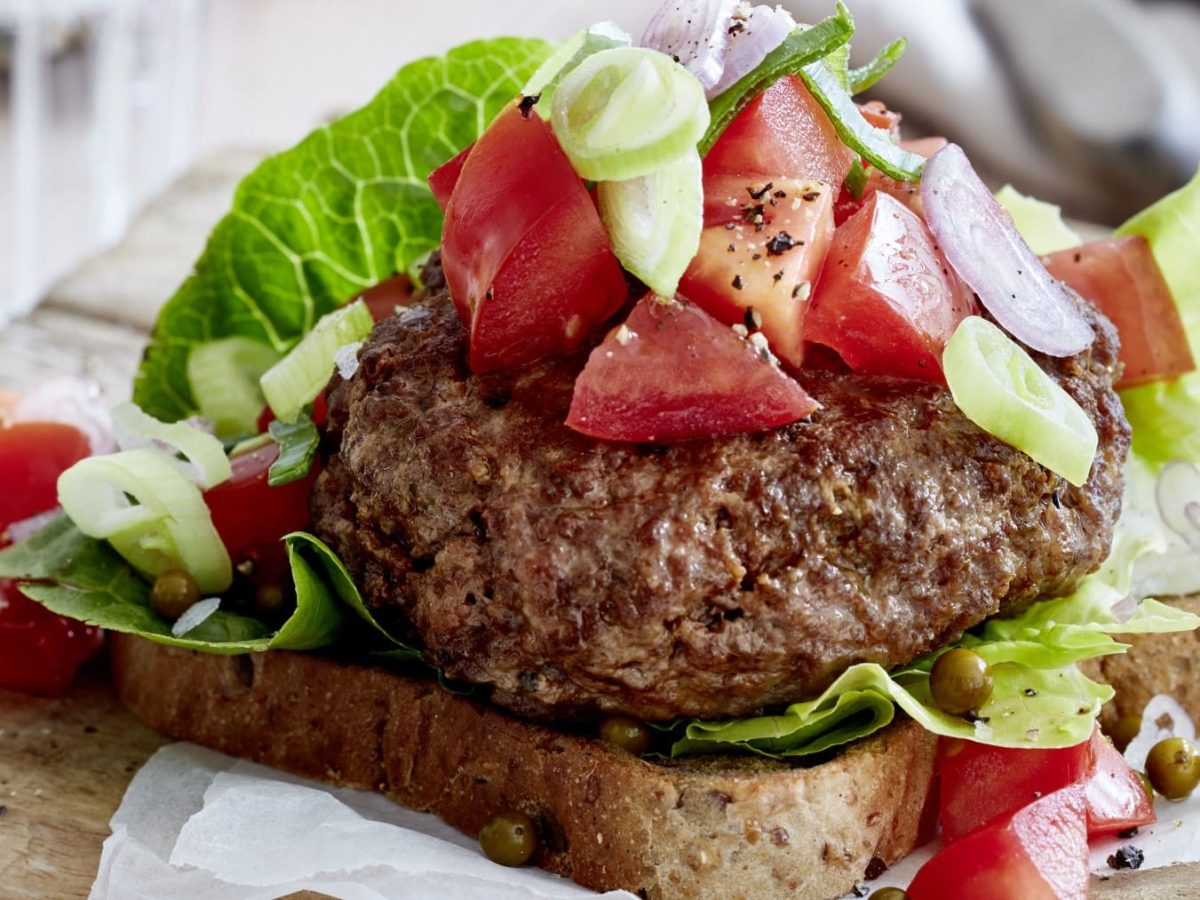 Ein leichter Beef-Burger mit grünem Pfeffer auf einem braunen Schneidebrett.