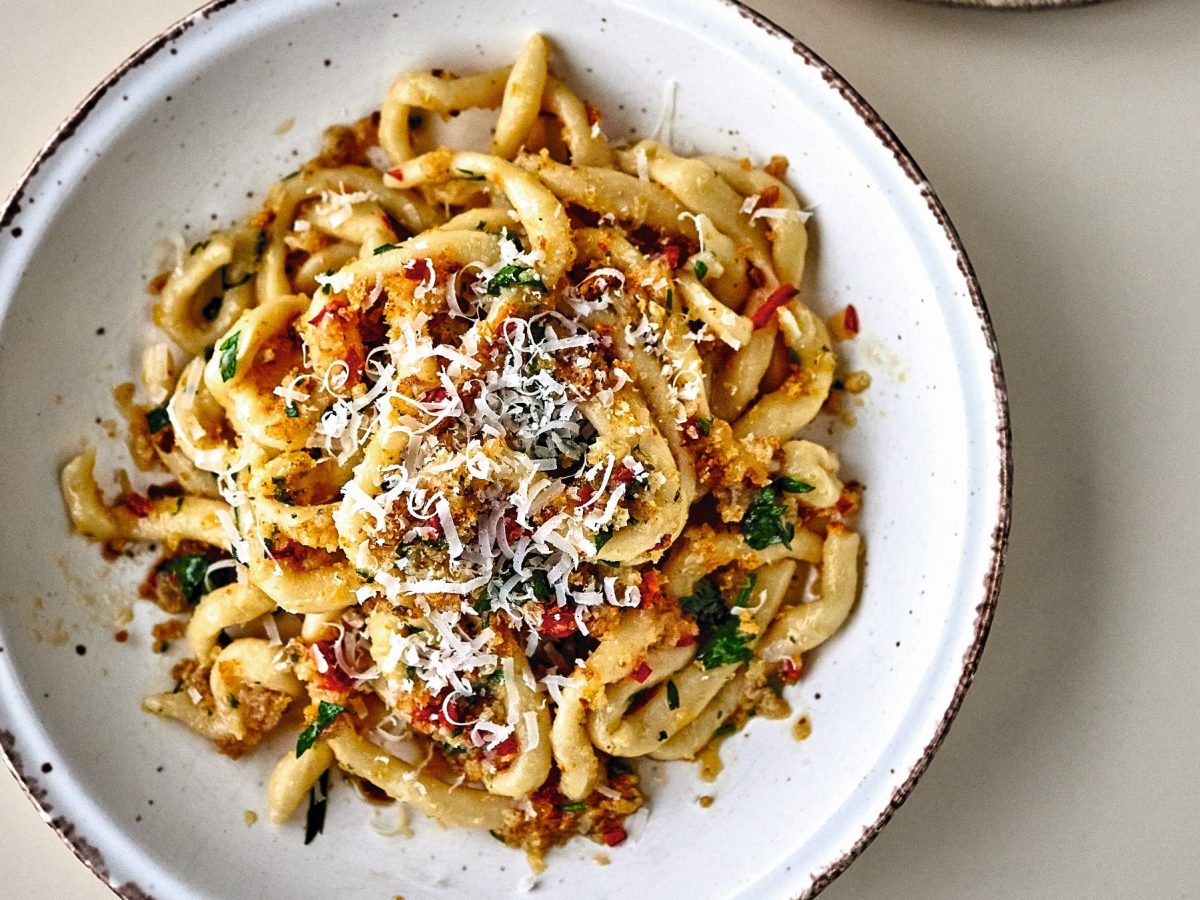 Ein weißer Teller mit der Pasta auf einem hellen Tisch direkt von oben fotografiert.