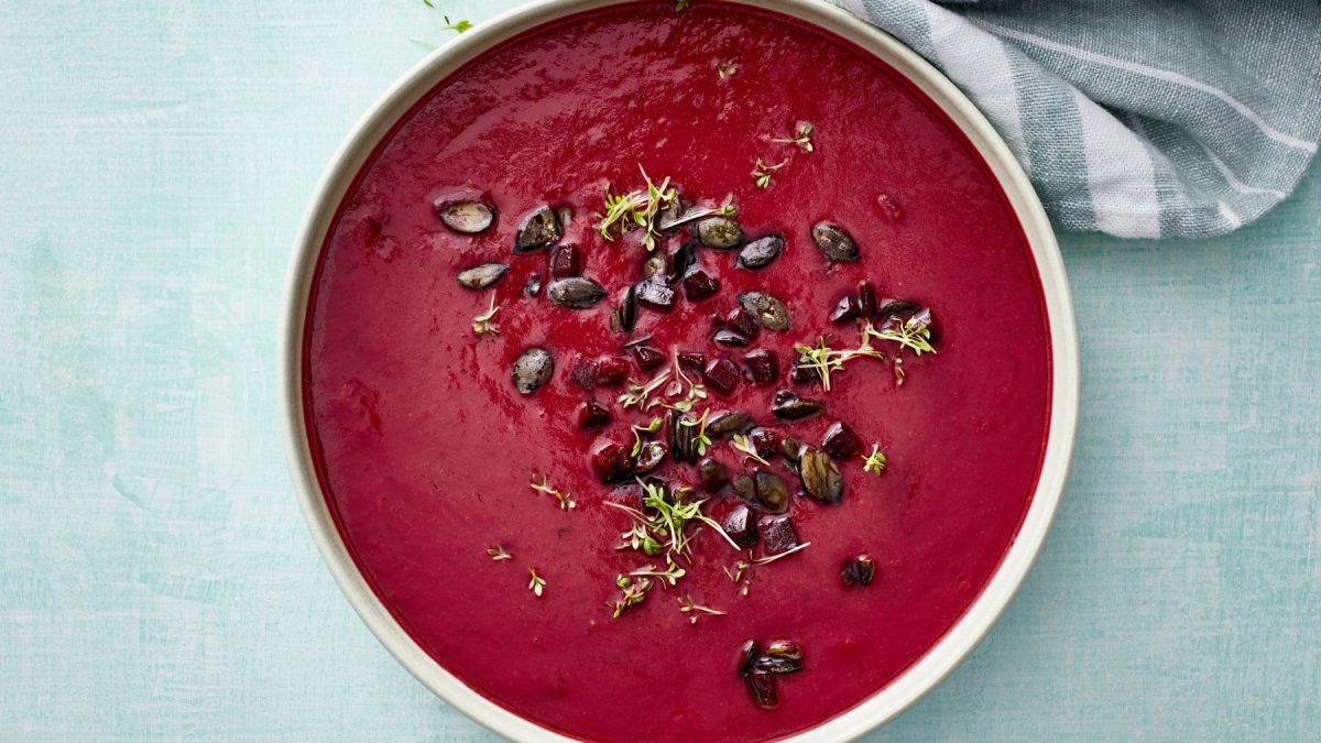 Eine Rote-Bete-Ingwer-Suppe in einer weißen Schüssel vor einem auf einem türkisen Hintergrund.