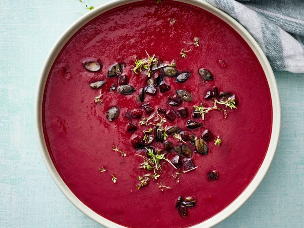 Eine Rote-Bete-Ingwer-Suppe in einer weißen Schüssel vor einem auf einem türkisen Hintergrund.