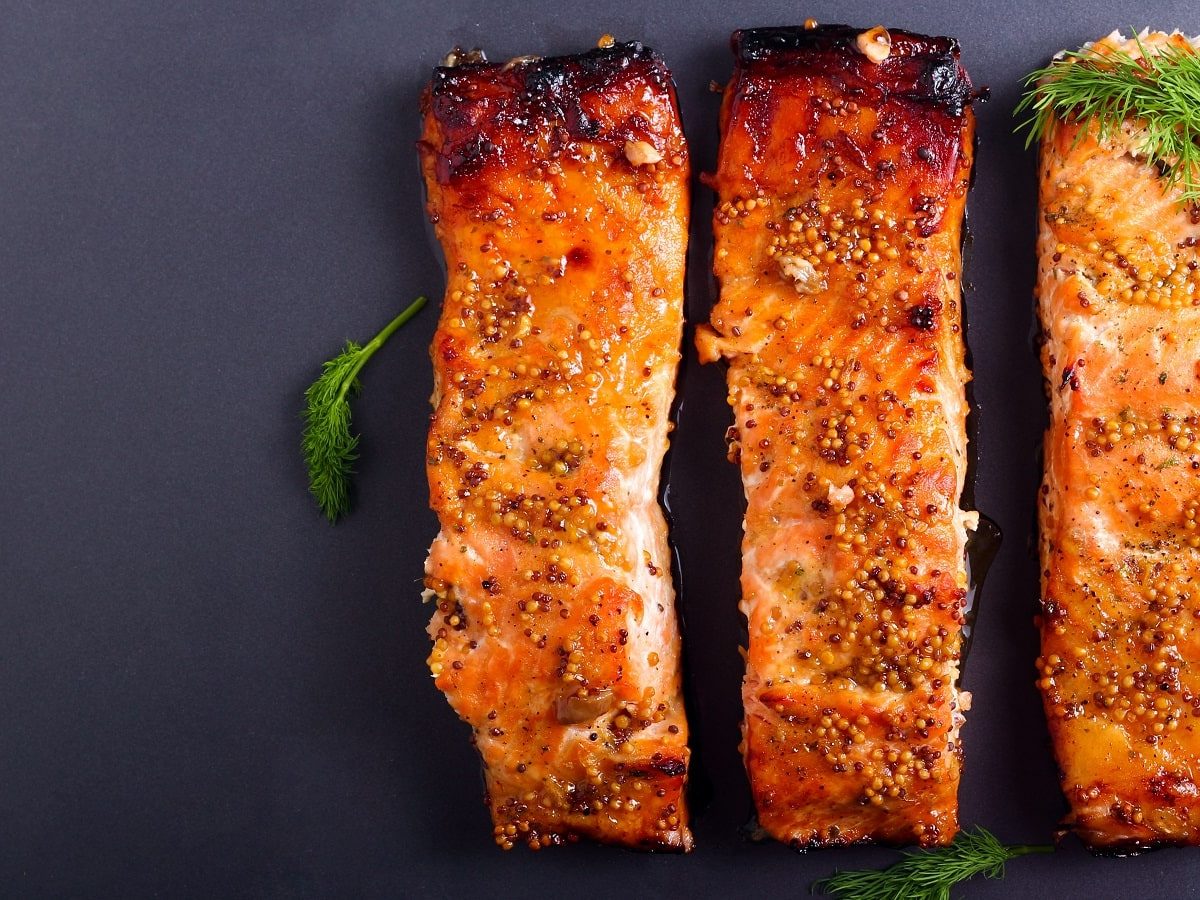 Drei Stück Honig-Senf-Lachs auf einem dunklen Untergrund.