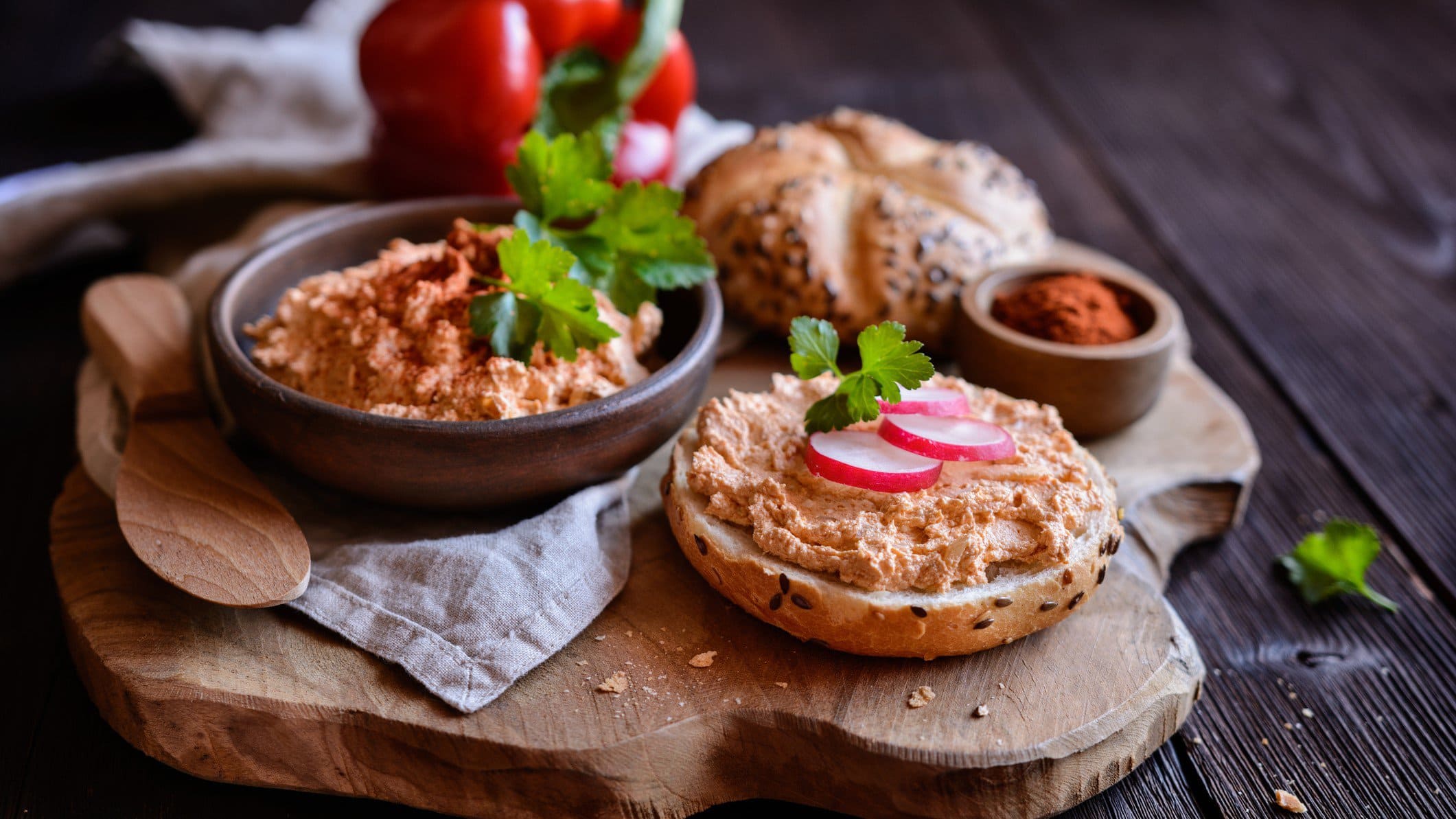 Original Spundekäs nach Winzerart aus Rheinhessen und Hessen in schwarzer Schale und auf Brötchen auf Holz und dunklem Untergrund. Im Bild Radieschen, Paprika und ein Schälchen Paprikapulver. Draufsicht.