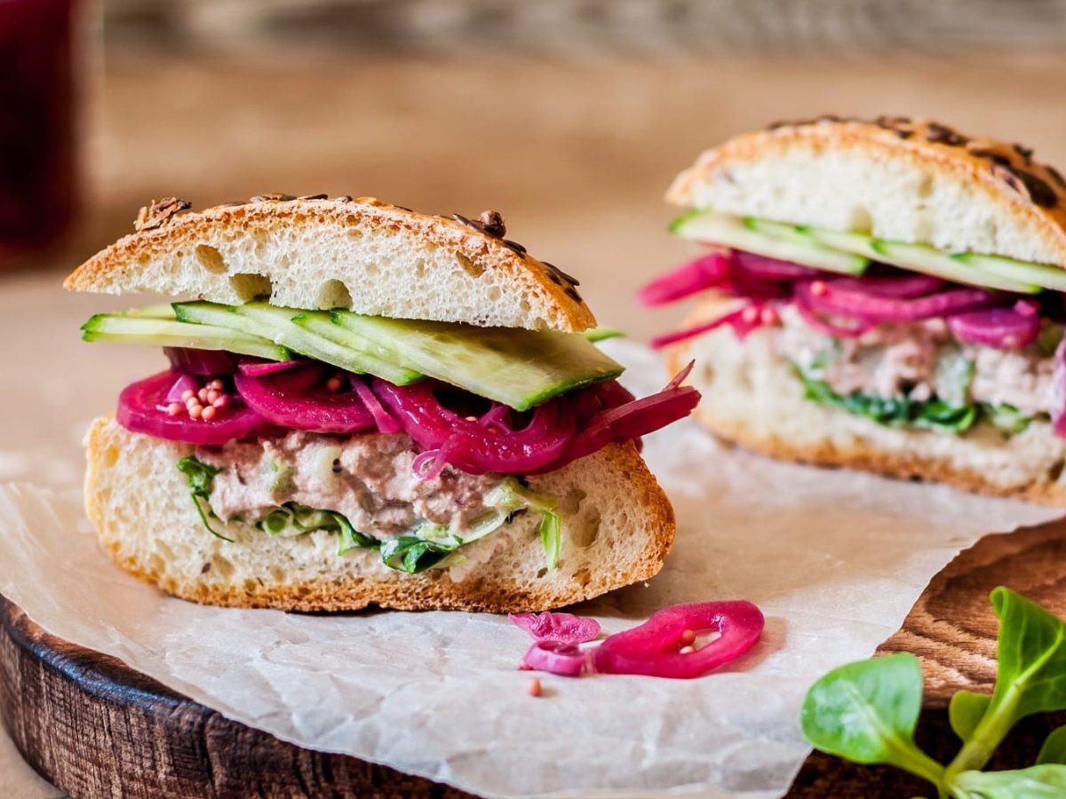 Ein halbiertes Brötchen mit Gurke, Thunfisch und roten Zwiebeln.