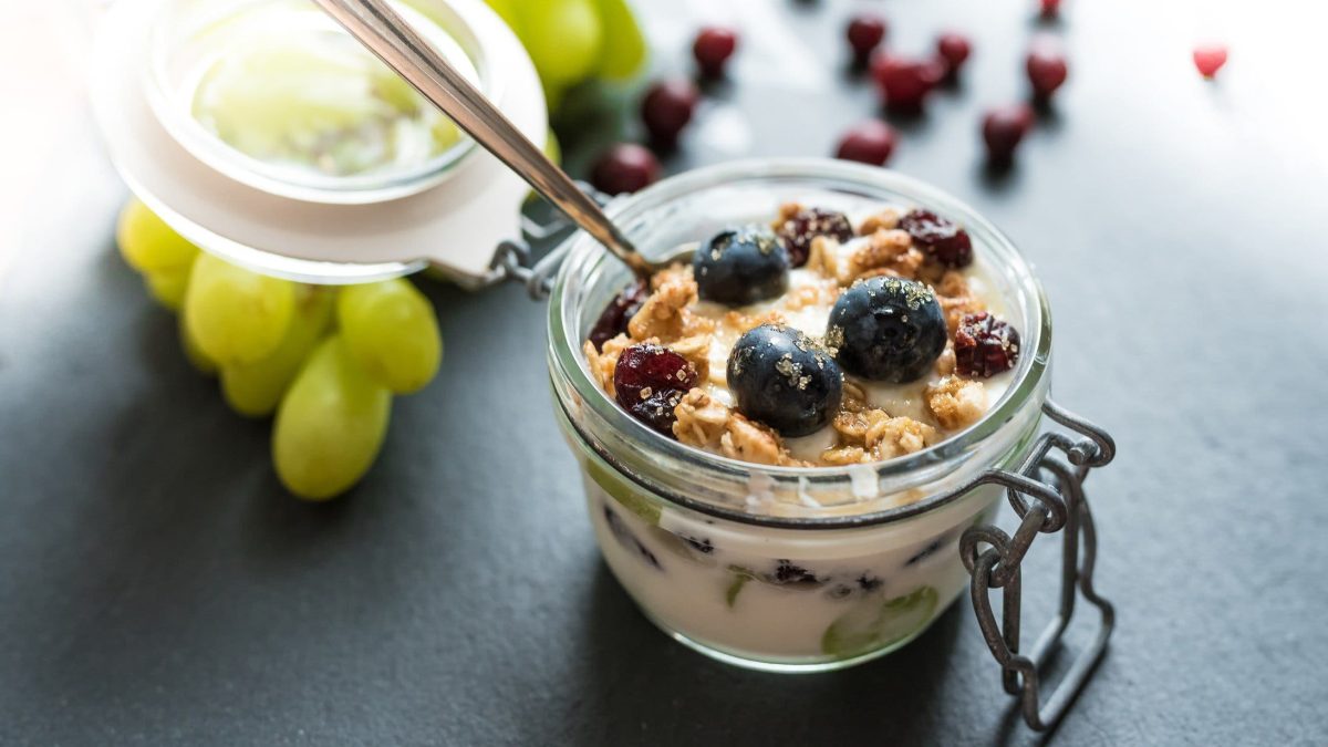 Traubendessert mit Hafer-Cookie-Crumble mit Vanillecreme und Beerenmix im Glas auf dunklem Untergrund. Im Bild eine Glasschale mit Trauben. Im BIld Beeren und Hafercrumble. Draufsicht.