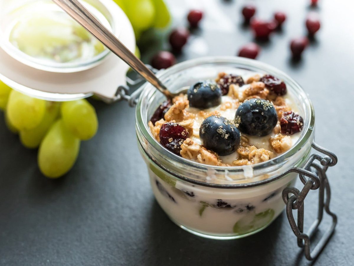 Traubendessert mit Hafer-Cookie-Crumble mit Vanillecreme und Beerenmix im Glas auf dunklem Untergrund. Im Bild eine Glasschale mit Trauben. Im BIld Beeren und Hafercrumble. Draufsicht.