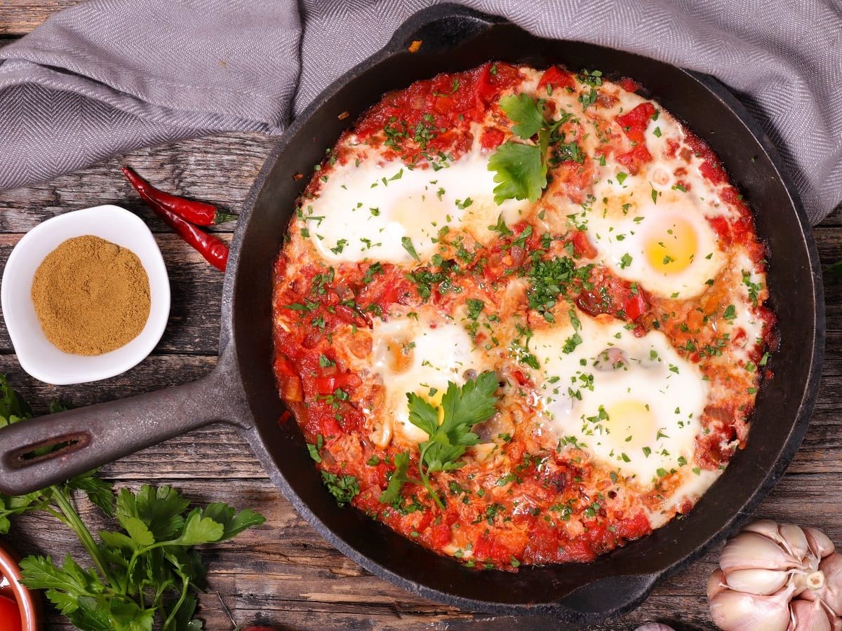 Eine schwarze gusseiserne Pfanne mit koreanischem Shakshuka auf einem Holztisch.