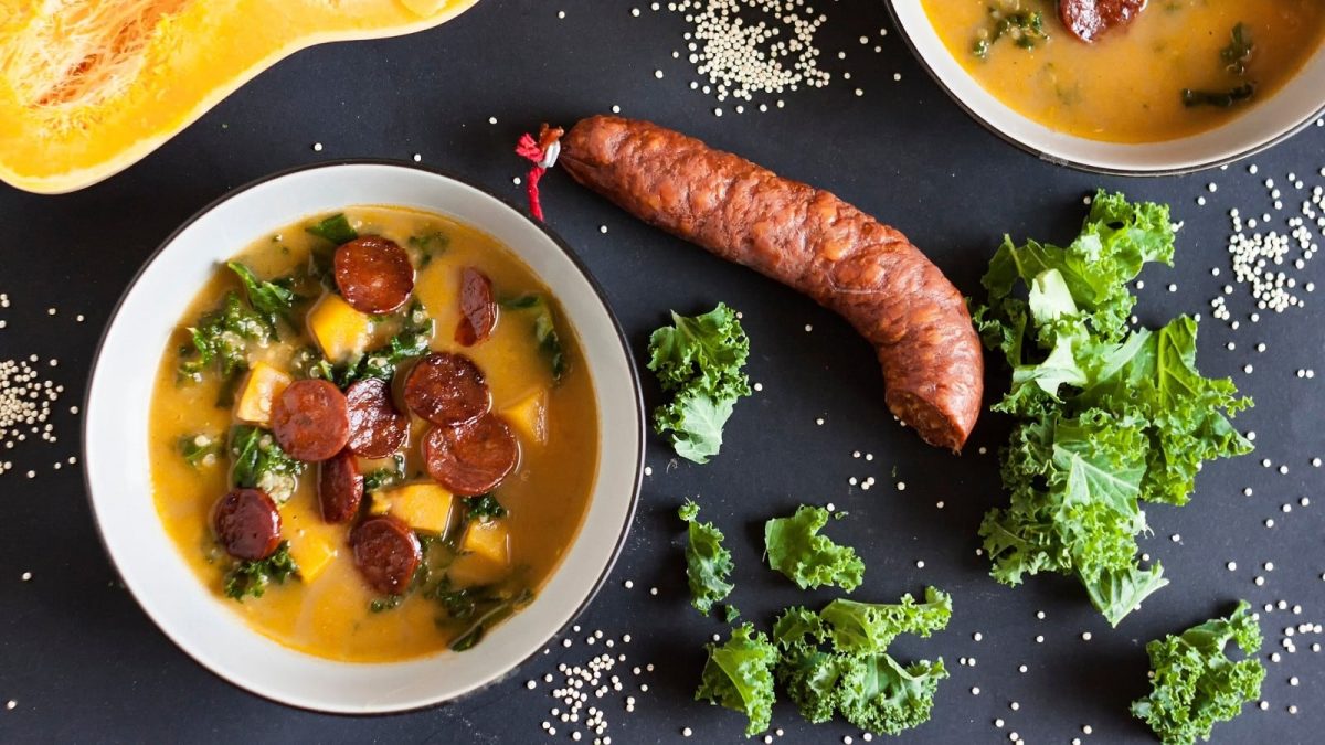 Eine weiße Suppenschüssel mit einer Portion Chorizo-Kürbissuppe auf einem dunklen Tisch.