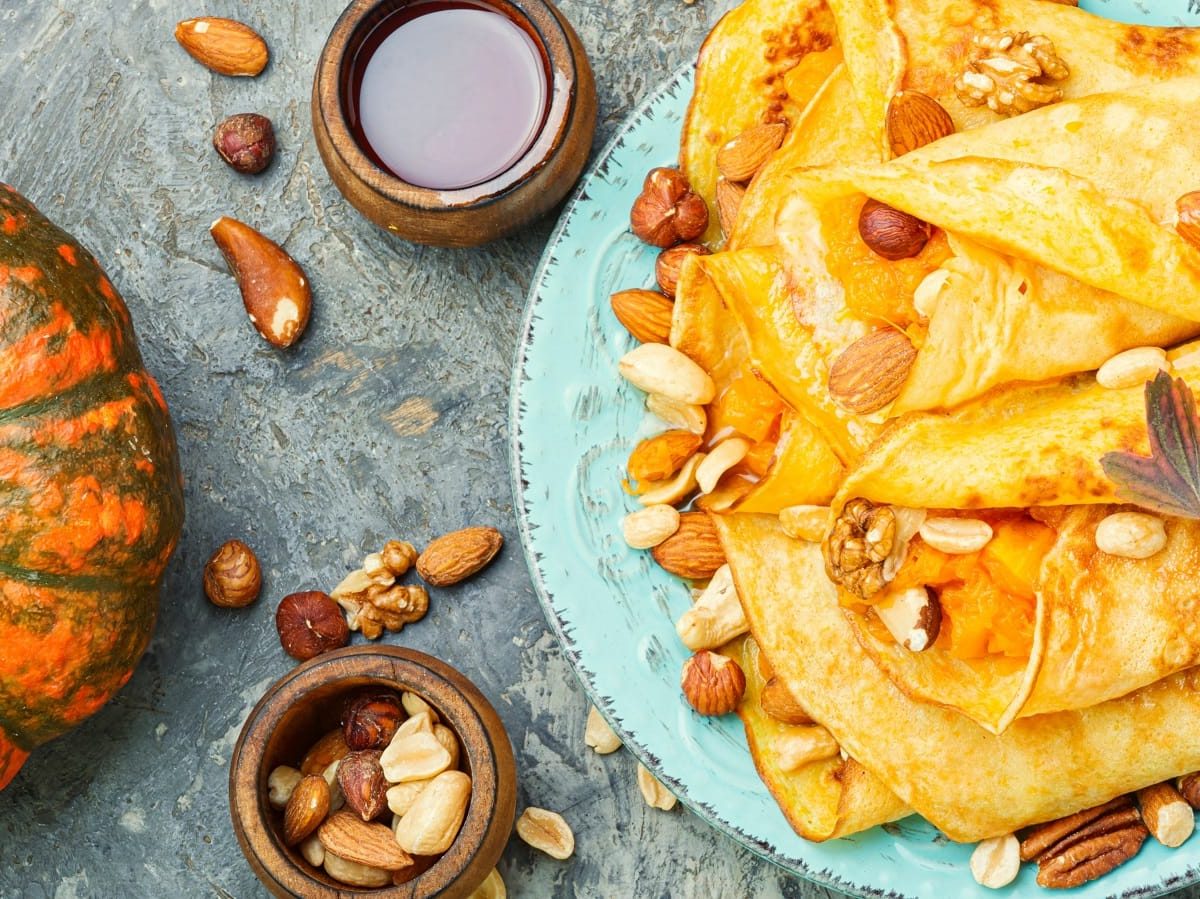 Ein türkiser Teller mit Kürbis-Crêpes neben einem frischen Kürbis.