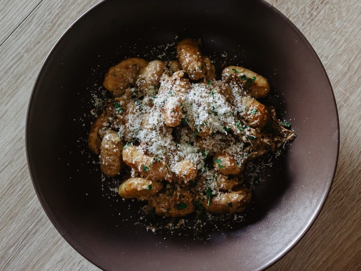 Ein brauner Teller mit Gnocchi in Nussbutter auf einem Holztisch.