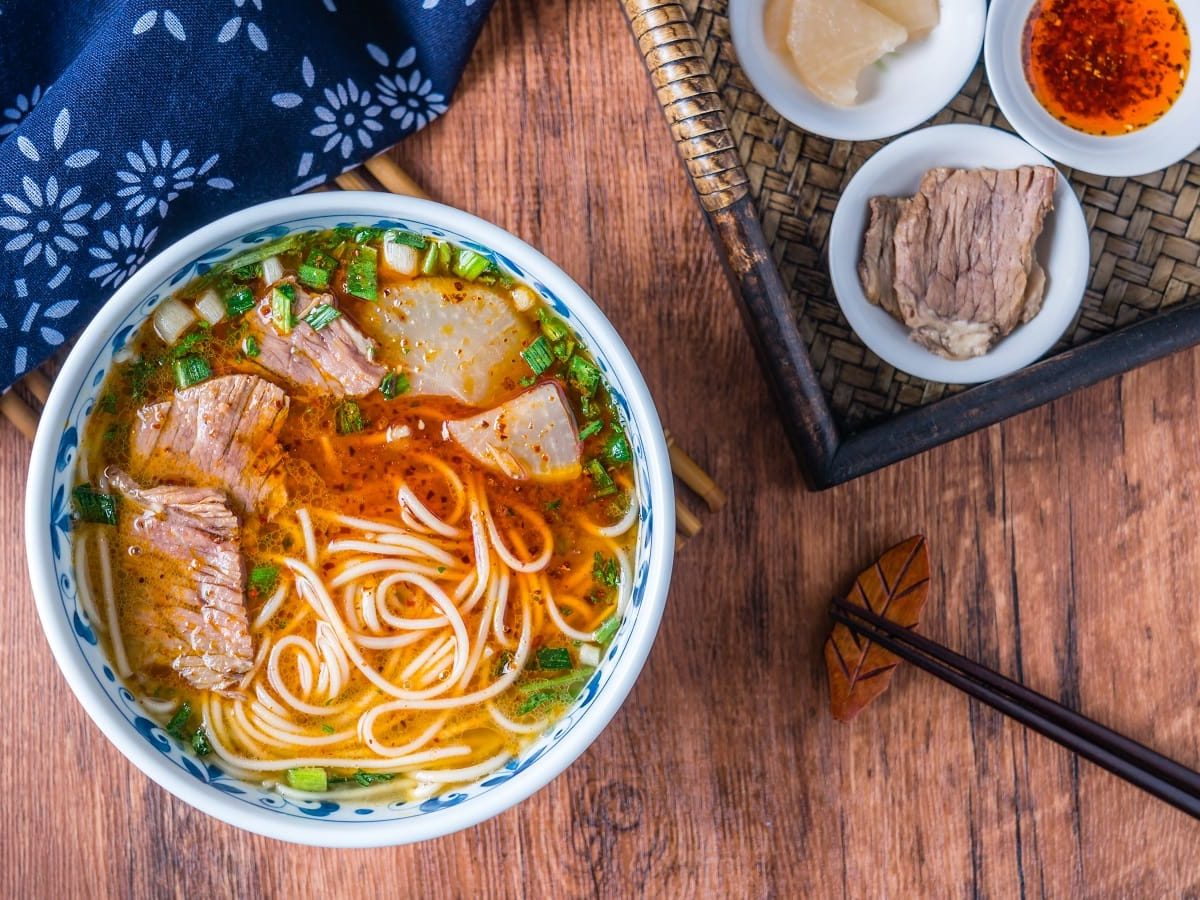 Eine Portion Lanzhou-Nudelsuppe n einer blauen Schüssel auf einem Holztisch.