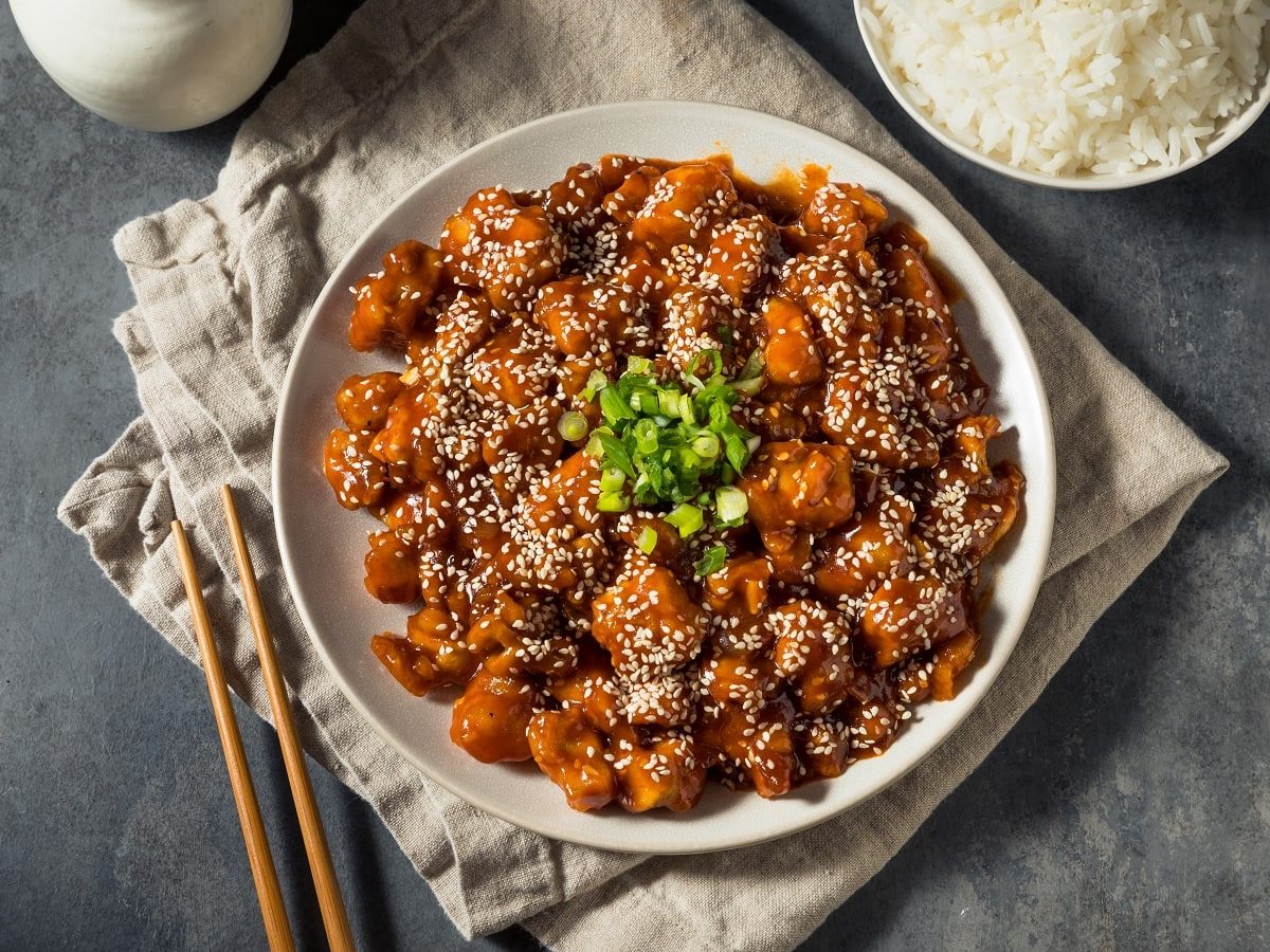 Ein weißer Teller mit Gochujang Chicken auf einem grauen Tisch.