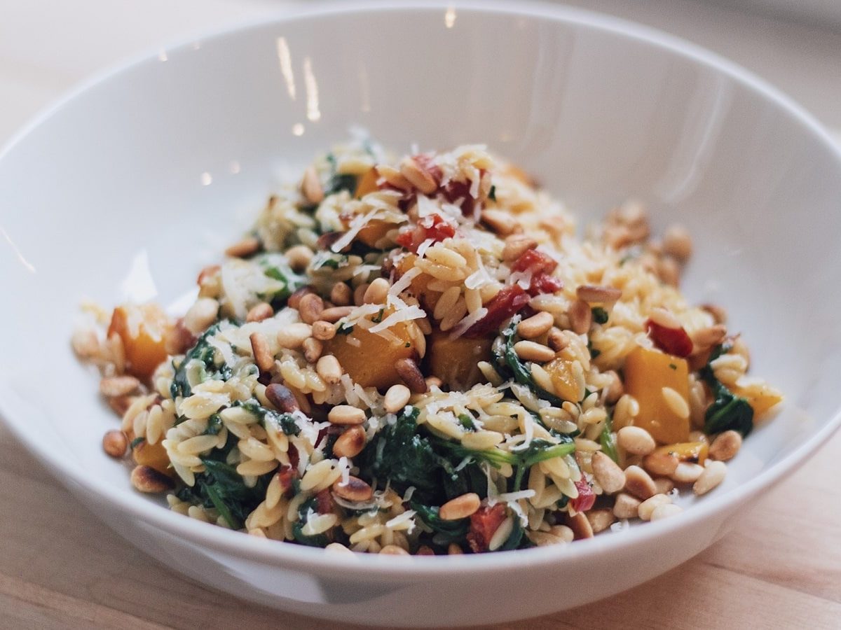 Ein weißer tiefer Teller mit einer Portion Orzo-Pfanne mit Kürbis und Spinat.