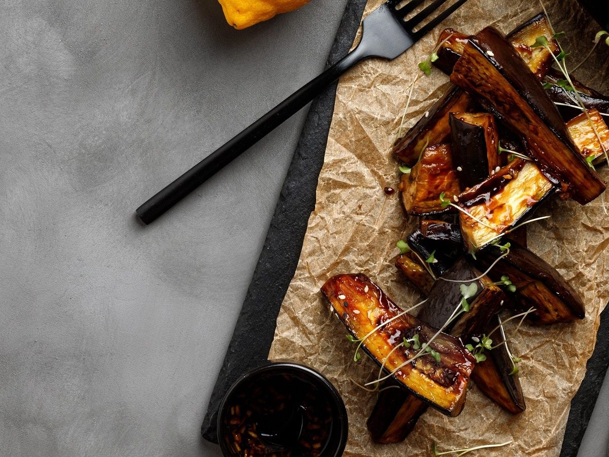 Ein schwarzes Schiefertablett mit Auberginen-Unagi auf einem grauen Tisch.