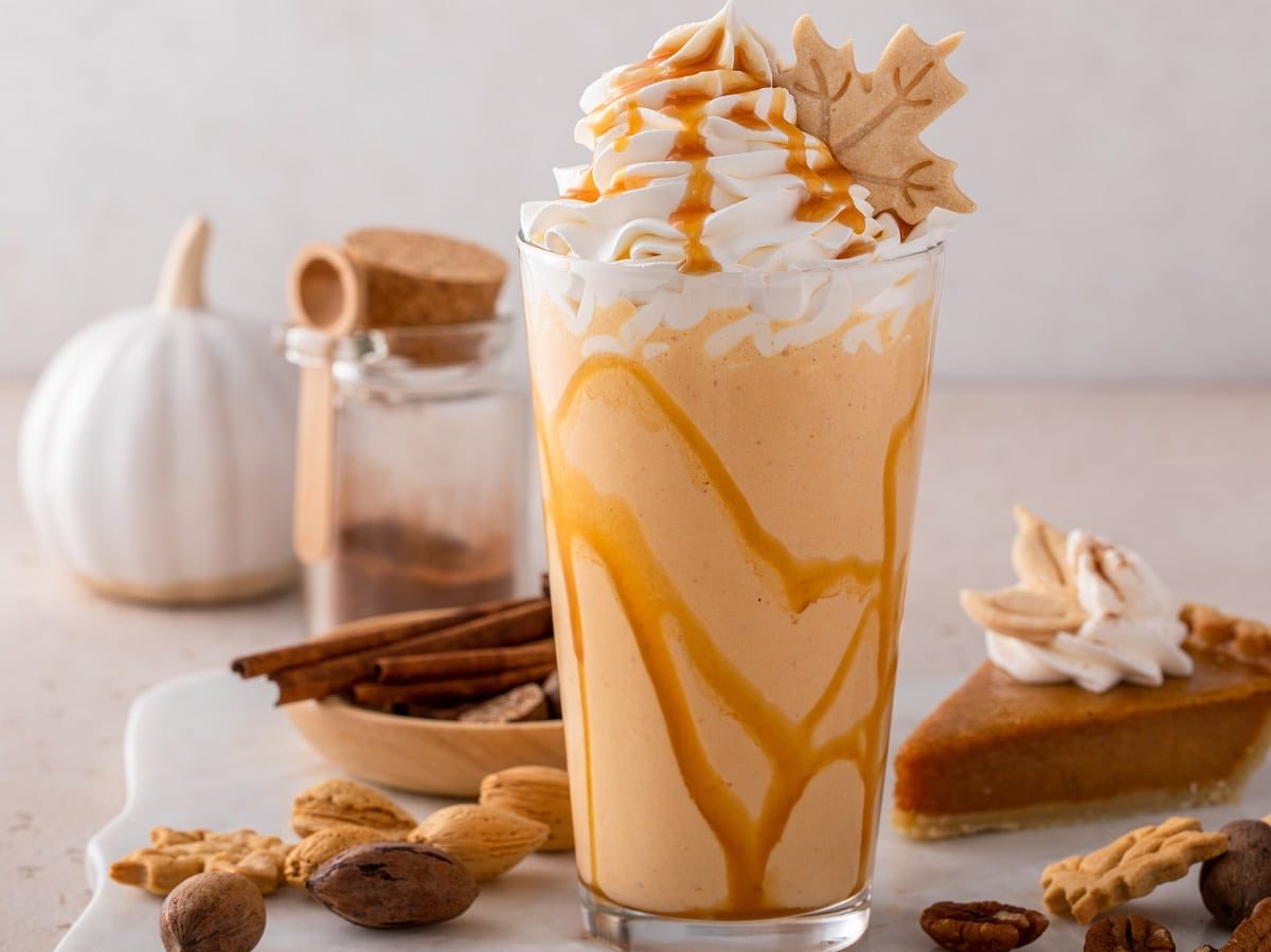 Ein Glas Pumpkin Spice Frappuccino neben einem Stück Pumpkin Pie.