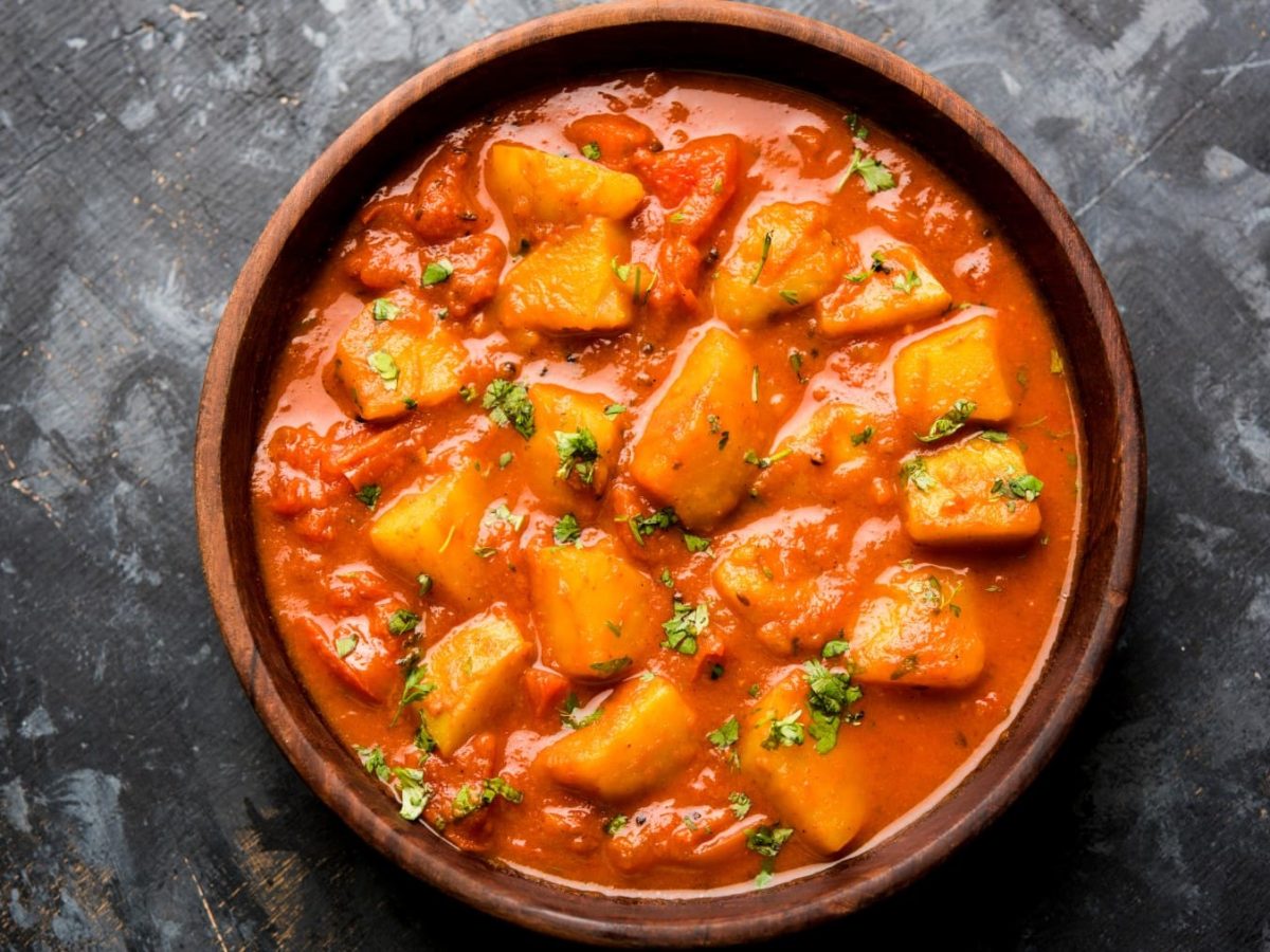 Aloo Madras in einer braunen Schüssel auf einem dunkelgrauen Hintergrund.