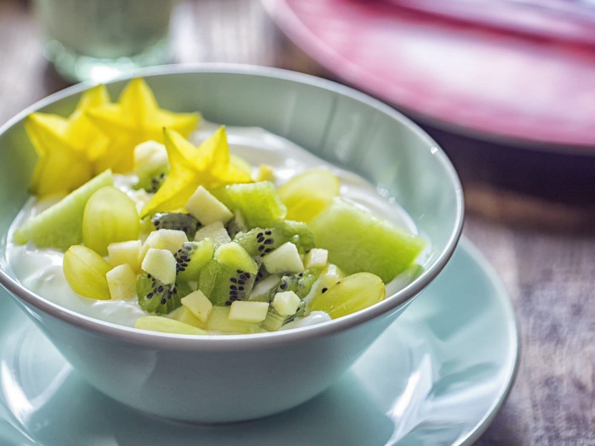 Draufsicht: ein Früchte-Frühstück mit Skyr in einer hellblauen Schüssel, die auf einem passenden Unterteller steht.