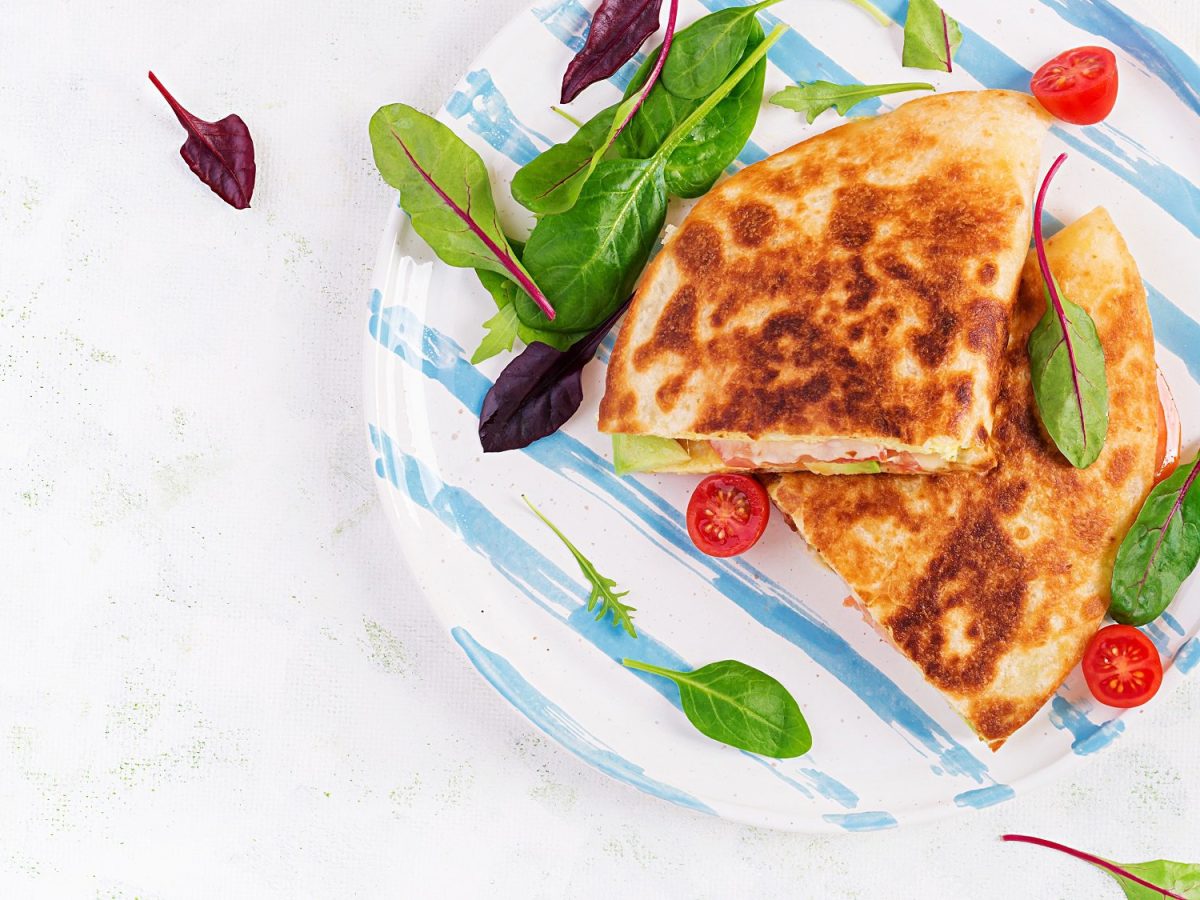 Getoastete Wraps mit Birne und Feta auf einem blau-weißen Teller in der Draufsicht, auf dem Teller liegen noch kleine halbierte Tomaten und ein paar Salatblätter.