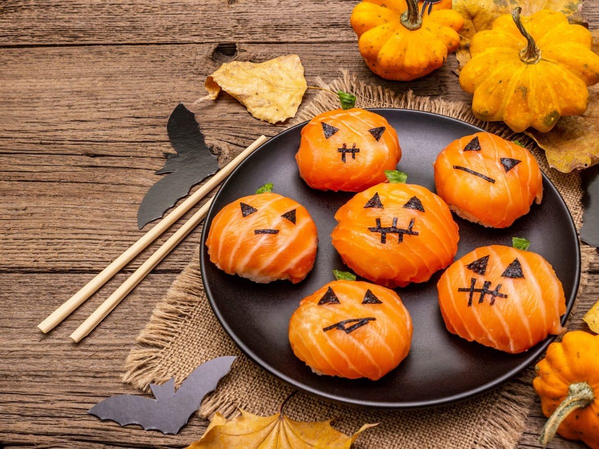 Ein schwarzer Teller mit dem Halloween Sushi auf einem rustikalem Holztisch von oben fotografiert.