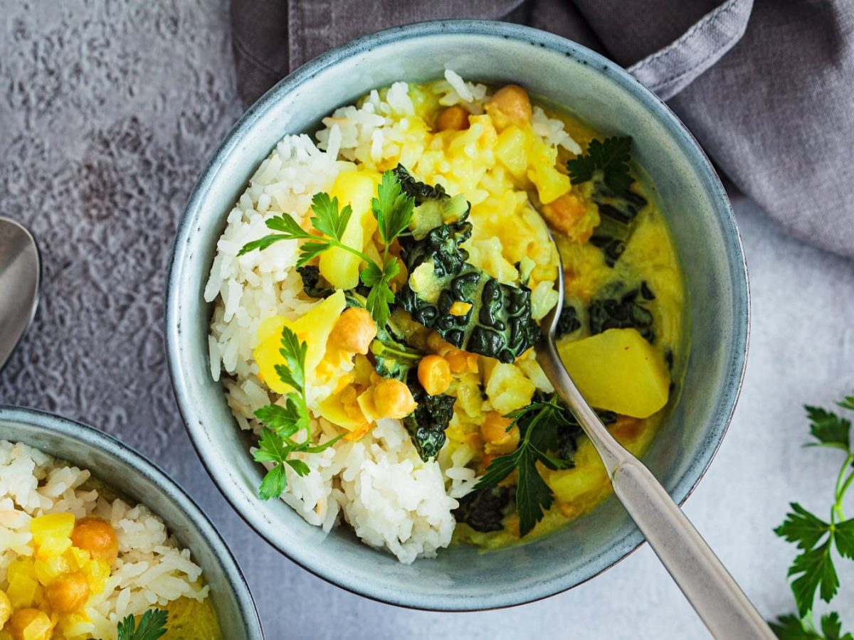 Eine hellblaue Schale mit dem Kartoffel-Curry auf grauem Untergrund direkt von oben fotografiert.