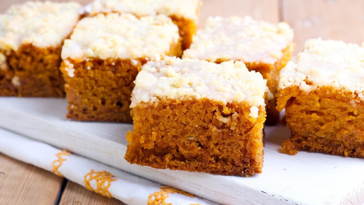 Mehrere Stücke Kürbiskuchen mit Kokostoppig auf einem weißen Holzbrett.