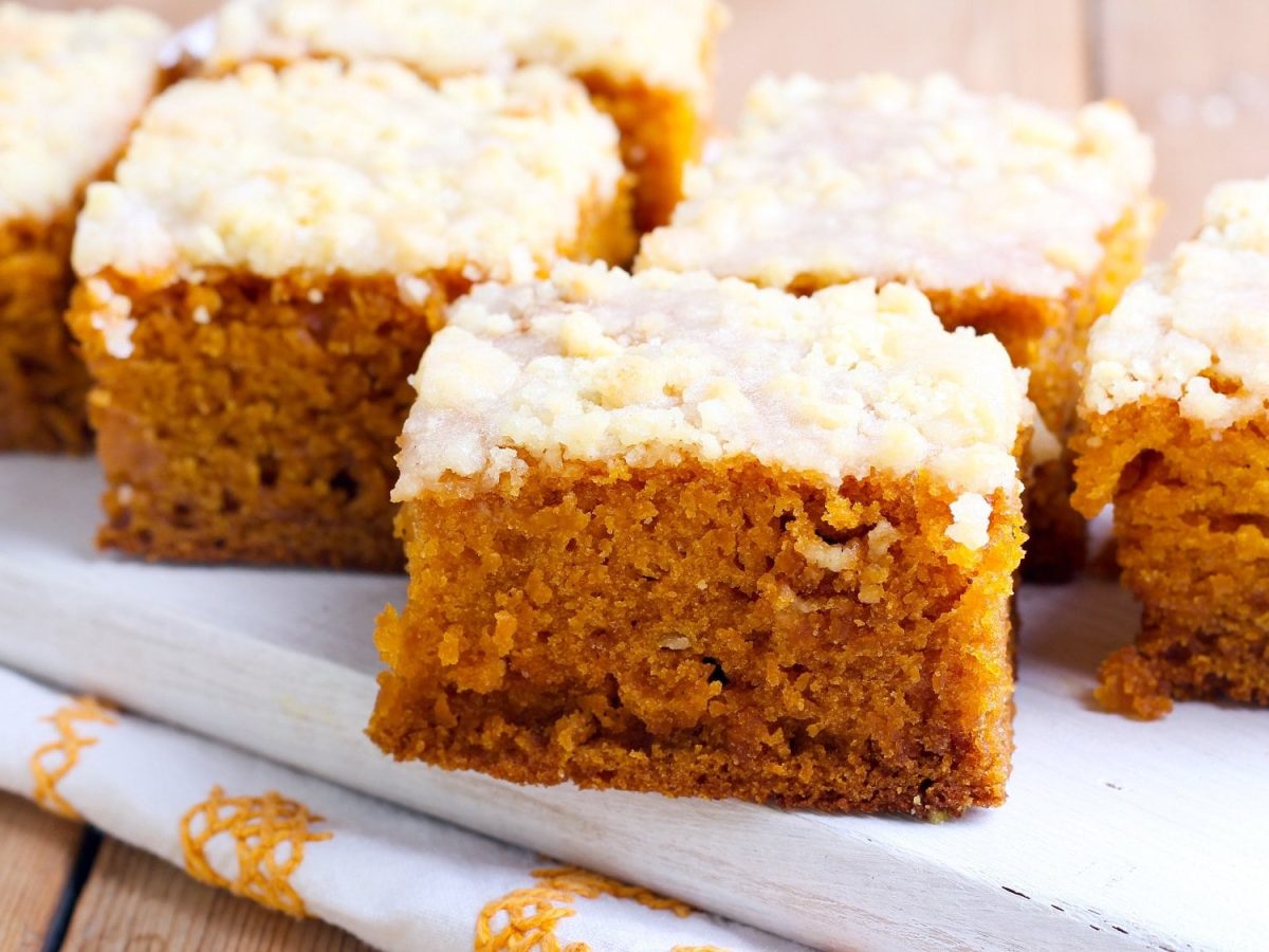 Mehrere Stücke Kürbiskuchen mit Kokostoppig auf einem weißen Holzbrett.