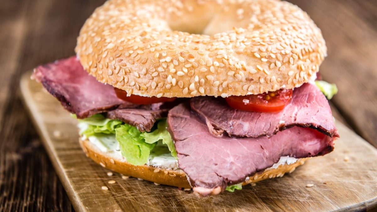 Draufsicht schräg: Ein Pastrami-Bagel auf einem Holzbrettchen.