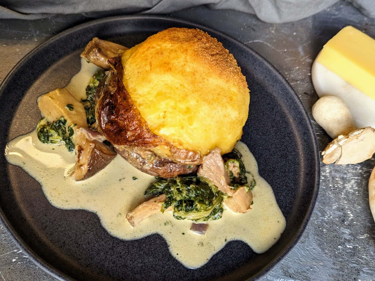 Ein schwarzer Teller mit dem Käse-Pilz-Knödel auf einem grauen Tisch von oben fotografiert.