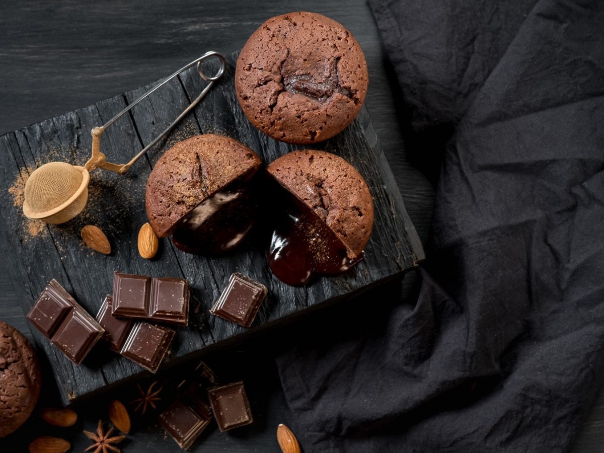 Schokokuchen mit flüssigem Kern auf dunklem Untergrund. Daneben ein schwarzes Tuch.