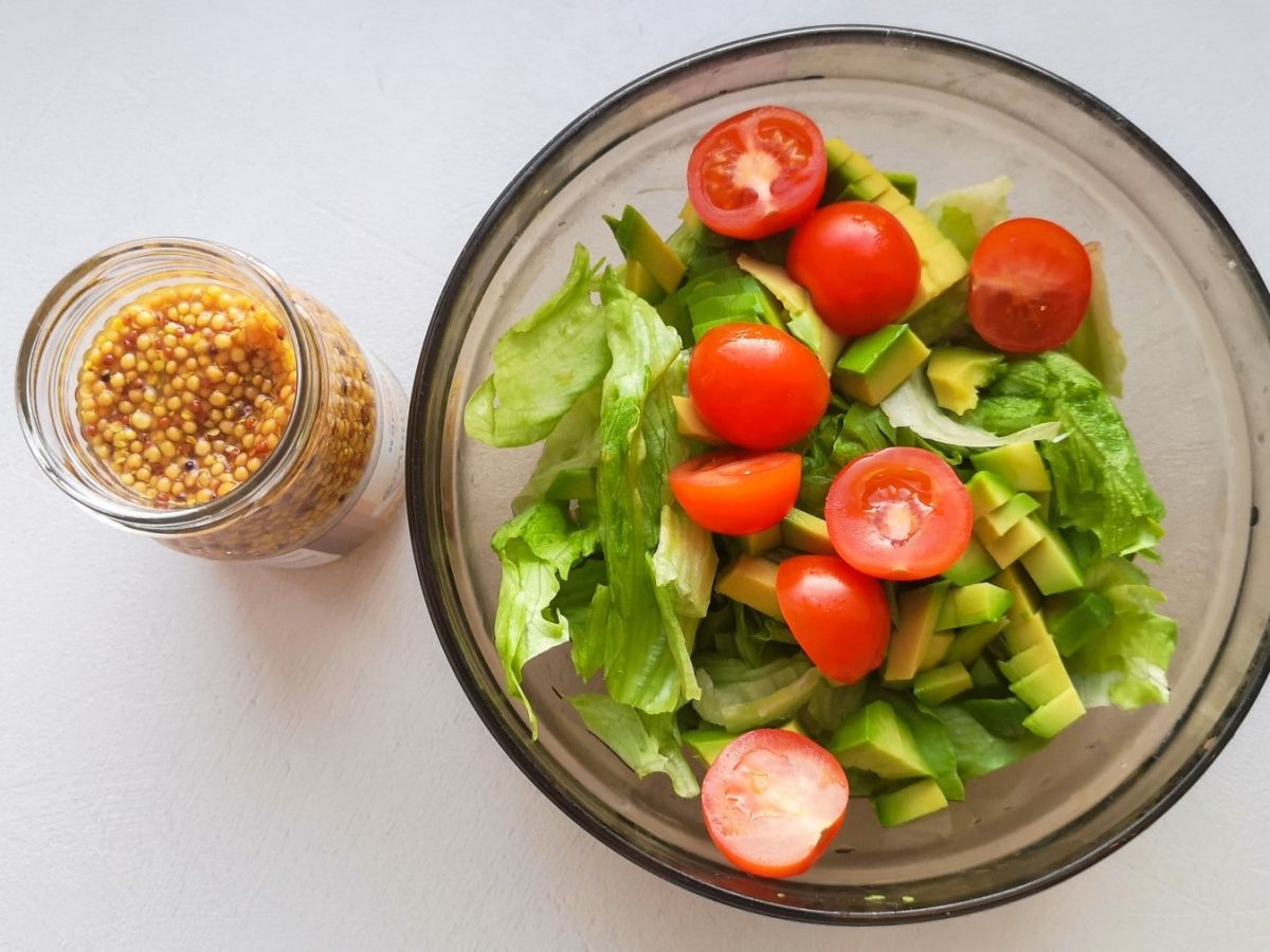 Senfkaviar in einem kleinen Glas. Rechts daneben eine Schüssel mit gemischten Salat. Der Hintergrund ist weiß.