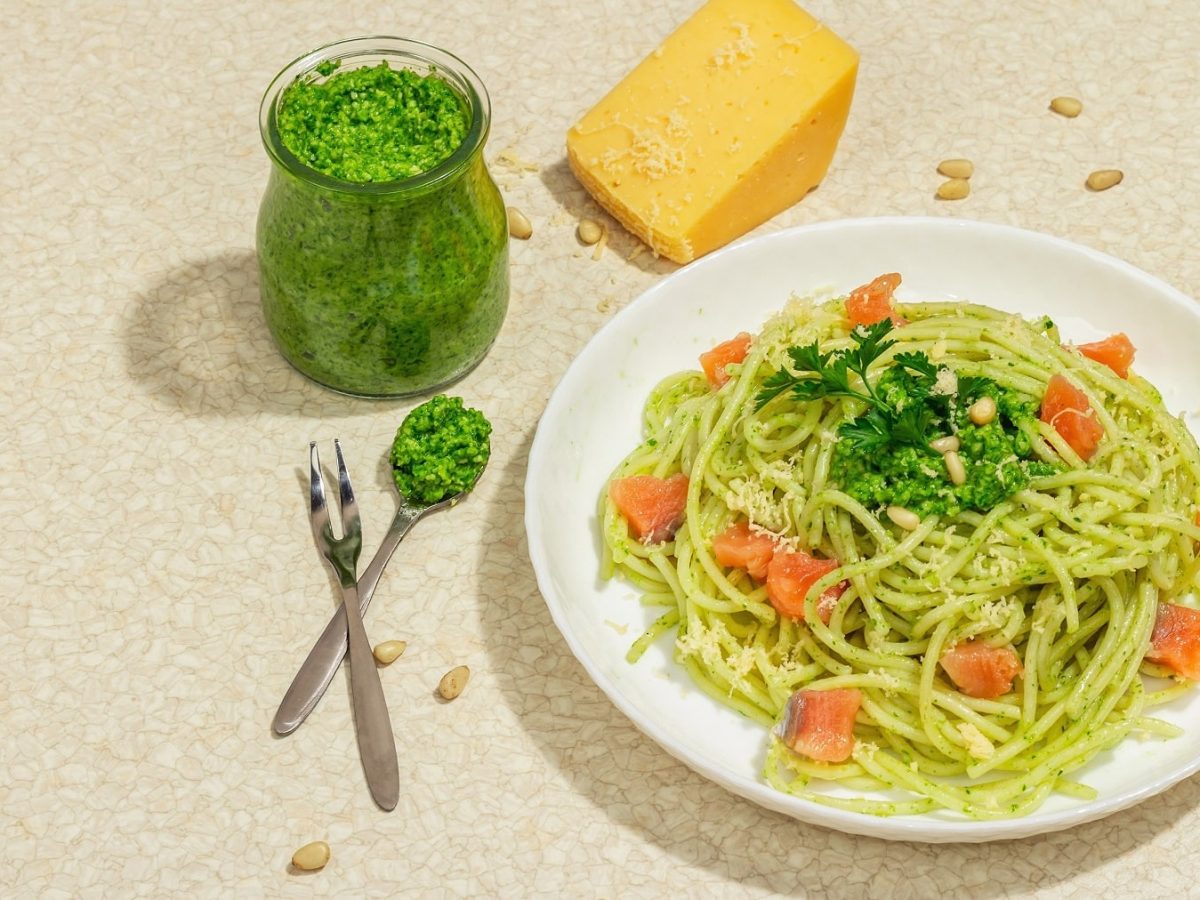 Ein weißer Teller mit den Spaghetti sowie Lachswürfeln und Lauch-Pesto auf beigem Untergrund.